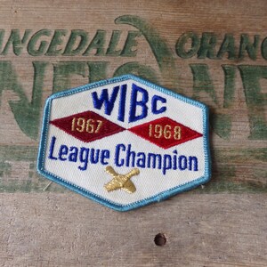 May include: Embroidered patch with a white background, blue trim, and the text "WIBc League Champion." Features red diamond shapes with the years 1967 and 1968. A gold bowling pin is at the bottom. The patch is on a wooden surface.