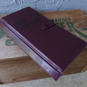 May include: A burgundy leather AAA Map-Pak binder with a globe logo and the text "Map-Pak" printed on the cover. The binder has a metal clasp and is made in the USA.