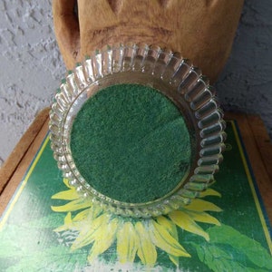 May include: A clear glass coaster with a scalloped edge and a green felt bottom.