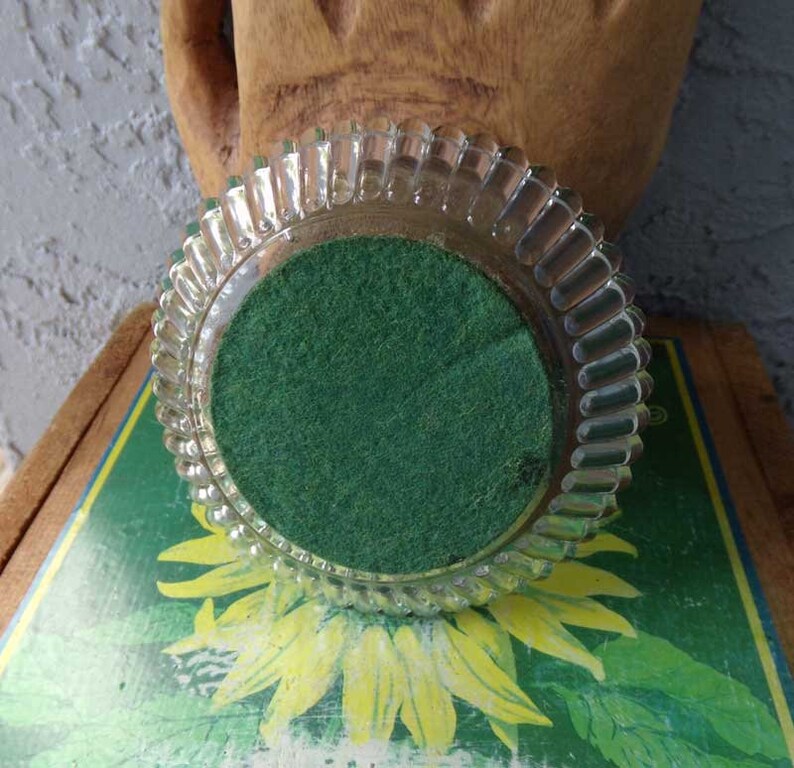 May include: A clear glass coaster with a scalloped edge and a green felt bottom.