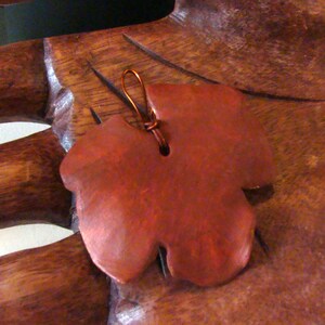 May include: A reddish-brown leaf-shaped pendant with a copper wire loop for hanging. The pendant has a smooth, polished surface and a naturalistic design, suggesting a nature-inspired jewelry piece.