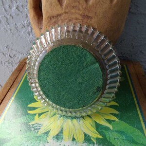 May include: A clear glass coaster with a scalloped edge and a green felt bottom.