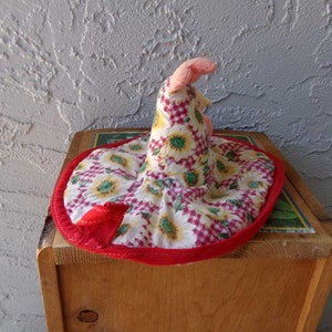 May include: A red and white fabric hat with a sunflower pattern. The hat has a pointed top and a wide brim. The hat is made of a soft, quilted fabric.