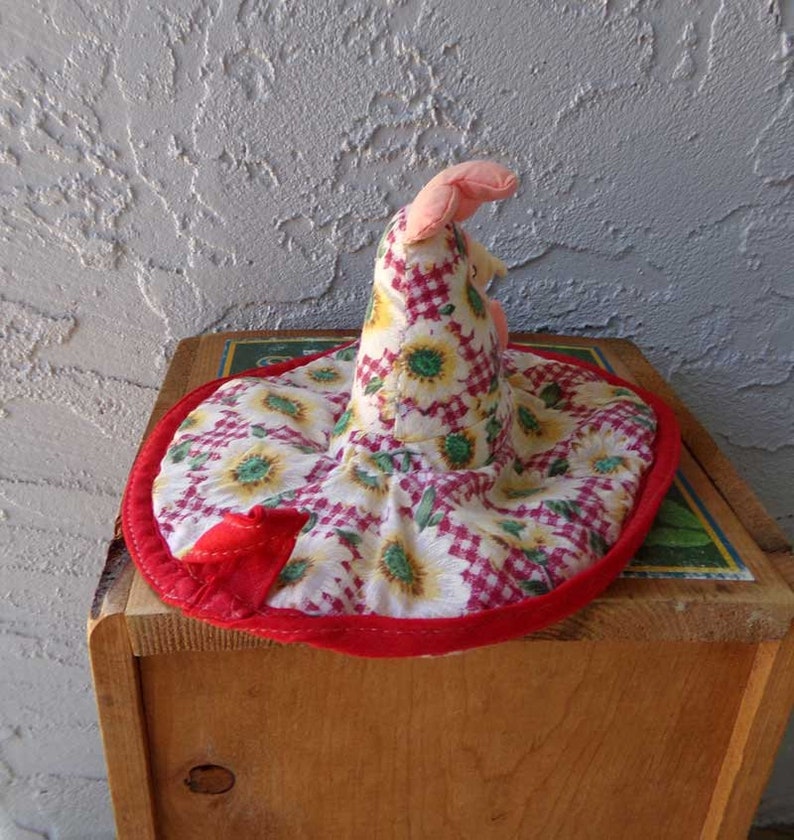 May include: A red and white fabric hat with a sunflower pattern. The hat has a pointed top and a wide brim. The hat is made of a soft, quilted fabric.
