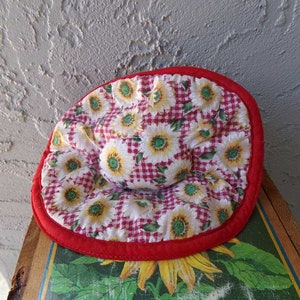 May include: Red and white pot holder with a sunflower and gingham pattern. The pot holder has a red border.
