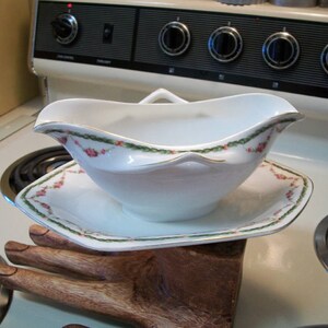 May include: A white porcelain gravy boat with a green and pink floral design. The boat is sitting on a matching saucer.