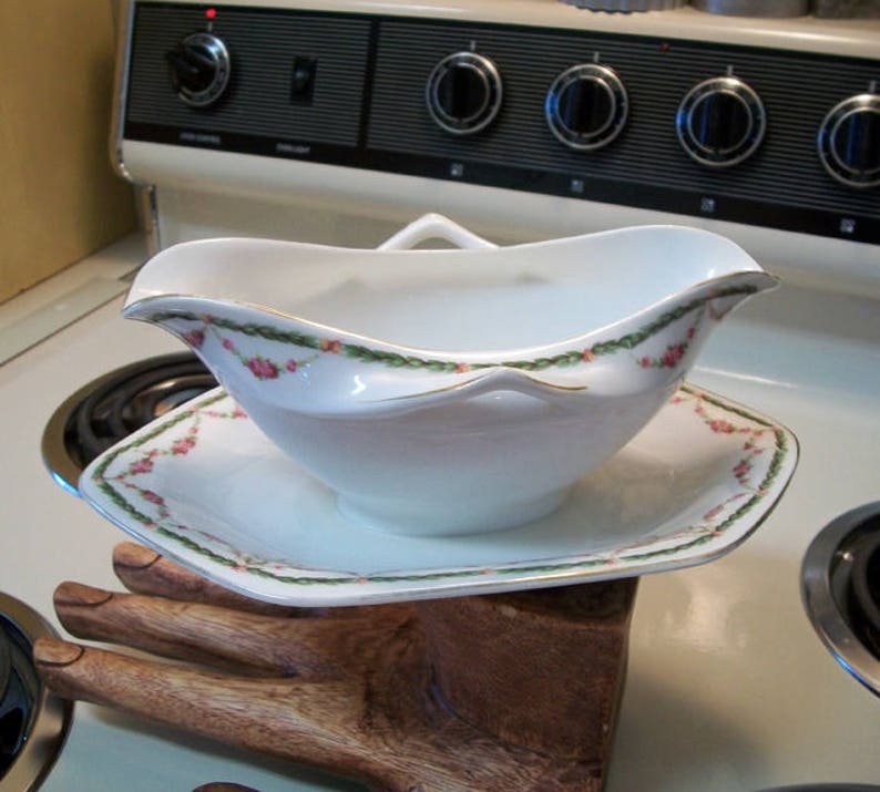 May include: A white porcelain gravy boat with a green and pink floral design. The boat is sitting on a matching saucer.