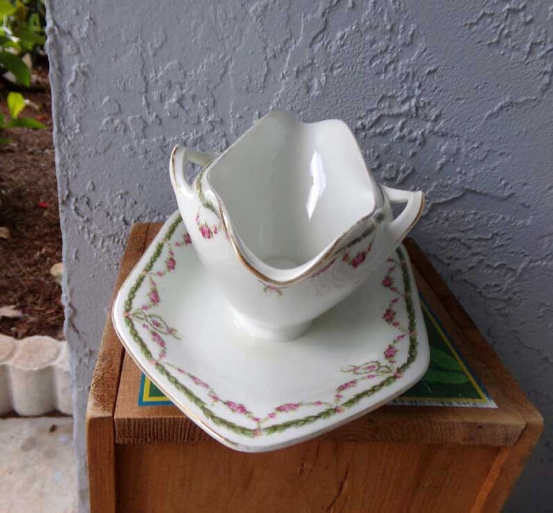 May include: White porcelain gravy boat with a gold trim and a floral design. The boat is on a matching saucer with a green and pink floral design.