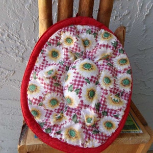 May include: Red and white fabric pot holder with a gingham pattern and a floral design. The pot holder is round and has a red border.