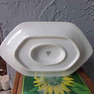 May include: White porcelain serving dish with a scalloped edge and a small, round indentation in the center. The bottom of the dish has a green and white mark.