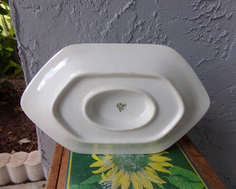 May include: White porcelain serving dish with a scalloped edge and a small, round indentation in the center. The bottom of the dish has a green and white mark.