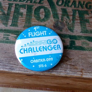 May include: A blue and white button with the text "1st Flight GO CHALLENGER" and "ORBITER-099 STS-6".