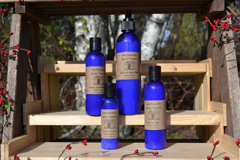 K&ouml;nnte beinhalten: Vier blaue Flaschen K&ouml;rperlotion mit wei&szlig;en Etiketten. Die Etiketten tragen den Text "Northwoods Body Treats" und die Namen der D&uuml;fte: "Honey Cacao Milk", "Boyficio Macadamia", "Secret Love" und "White Cedar".