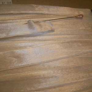May include: A close-up of a white, silky ribbon with a pin holding it in place. The ribbon is folded and has a slight sheen.