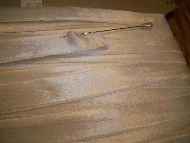 May include: A close-up of a white, silky ribbon with a pin holding it in place. The ribbon is folded and has a slight sheen.