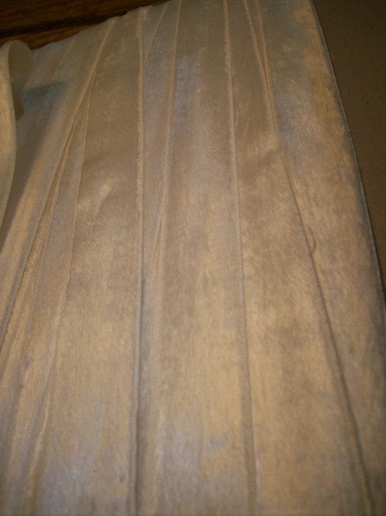 May include: White satin ribbon with vertical pleats. The ribbon has a subtle sheen and a smooth texture.