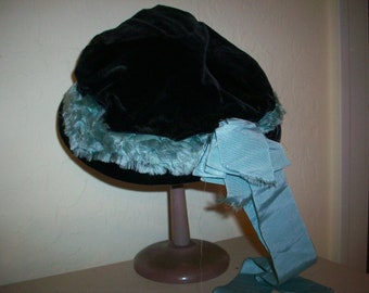 Puede incluir: Un sombrero de terciopelo negro con una cinta de satén azul y un ribete de piel azul claro.
