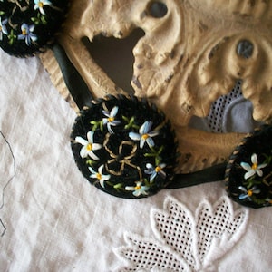 May include: A black velvet ribbon with three round black velvet ornaments embroidered with white and blue flowers.