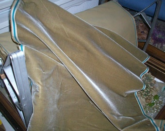 May include: A close-up of a beige velvet fabric with a white and teal trim. The fabric is folded and draped over a wooden surface.