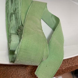 May include: A roll of soft, light green velvet ribbon. The ribbon is folded over itself, with a single length extending out. The ribbon has a slight sheen and a soft texture, perfect for crafts and embellishments.