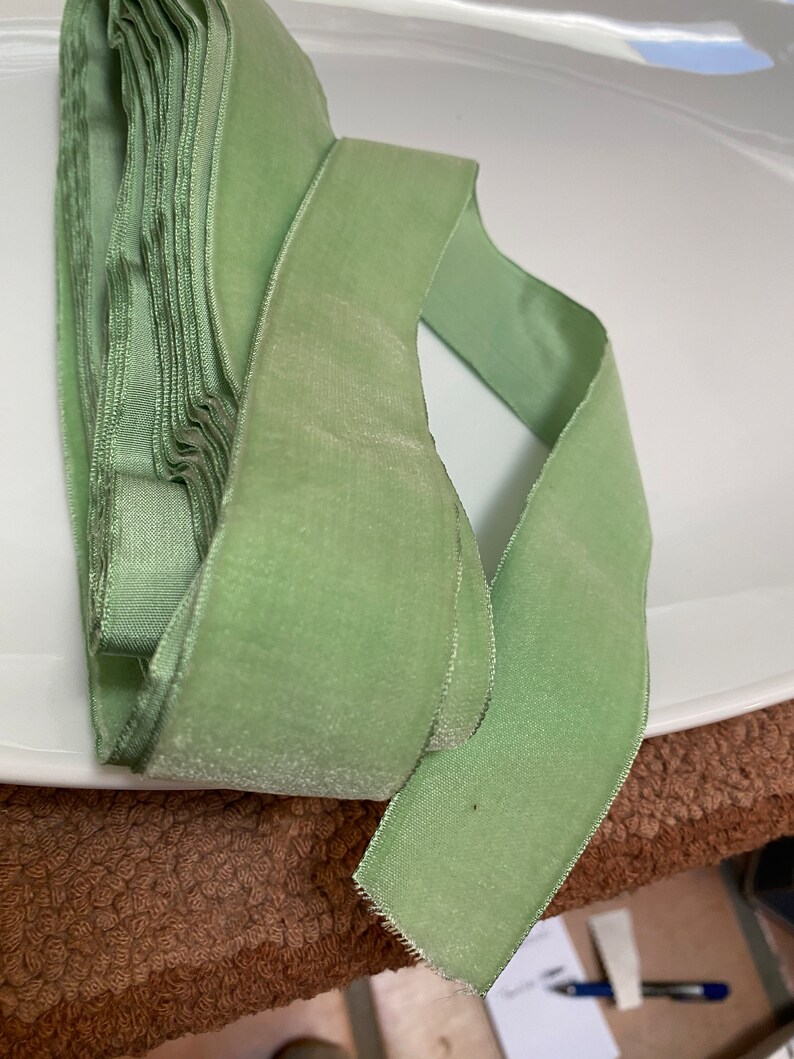 May include: A roll of soft, light green velvet ribbon. The ribbon is folded over itself, with a single length extending out. The ribbon has a slight sheen and a soft texture, perfect for crafts and embellishments.
