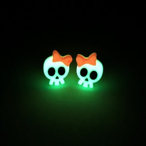 May include: A pair of glow-in-the-dark skull earrings with orange bows.