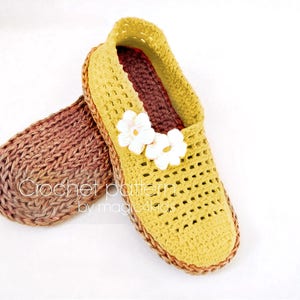 May include: A pair of crocheted slippers in yellow and brown. The slippers feature a flower design on the top and the text "Crochet pattern by magic4kid" is visible on the bottom.