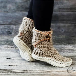 May include: Crocheted beige and white ankle boots with a brown button detail. The boots are worn by a person standing on a wooden floor. The text "Crochet pattern by magic4kids" is visible at the bottom of the image.