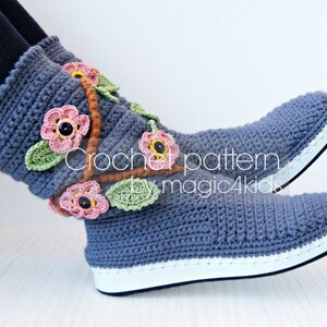May include: Crocheted blue slippers with a white sole and floral embellishments. The flowers are pink, orange, and green. The text "Crochet pattern by magic4kids" is visible on the slippers.