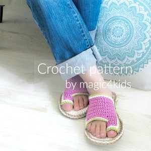 May include: Crochet pattern for pink and green sandals with a toe loop. The sandals are worn by a person sitting on a white cushion with a blue mandala pattern. The text "Crochet pattern by magic4kids" is visible below the sandals.