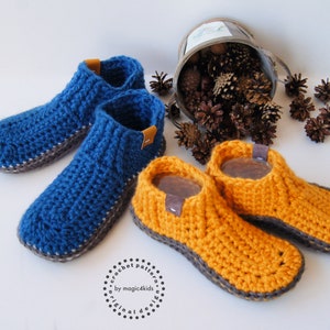 Peut inclure: Deux paires de chaussons crochetés à la main. L'une est bleue, l'autre orange. Les deux ont des semelles grises et de petites étiquettes en cuir marron. Les chaussons sont présentés sur une surface blanche. Le texte "crochet pattern by magic4kids original design" est visible.