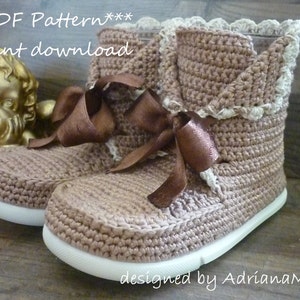 May include: A pair of brown crocheted booties with white crocheted trim and a brown satin ribbon. The booties have a white sole and are designed by AdrianaM.