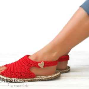 May include: Red crochet sandals with a heart-shaped button on the ankle strap. The sandals are on a white wooden surface.