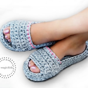 Op de afbeelding: Een paar grijze gehaakte slippers met roze bies. De slippers zijn open en hebben een eenvoudig ontwerp.