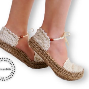 Puede incluir: Un par de sandalias de ganchillo con suela de yute y un lazo blanco. Las sandalias tienen un delicado borde de encaje y están hechas con hilo blanco. Las sandalias son un patrón de ganchillo de magic4kids.