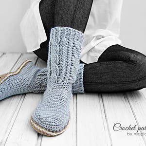Puede incluir: Un par de pantuflas de crochet azul claro con un ribete de crochet marr&oacute;n claro. Las pantuflas las lleva puestas una persona sentada en un suelo de madera. El texto "Crochet pattern by magic4kids" es visible en la parte inferior de la imagen.