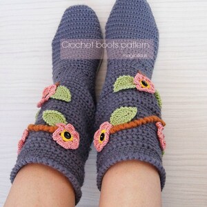 May include: A pair of gray crocheted boots with pink and green flower embellishments. The boots are designed by Adriana M. and are part of a crochet boots pattern by magic4kids.