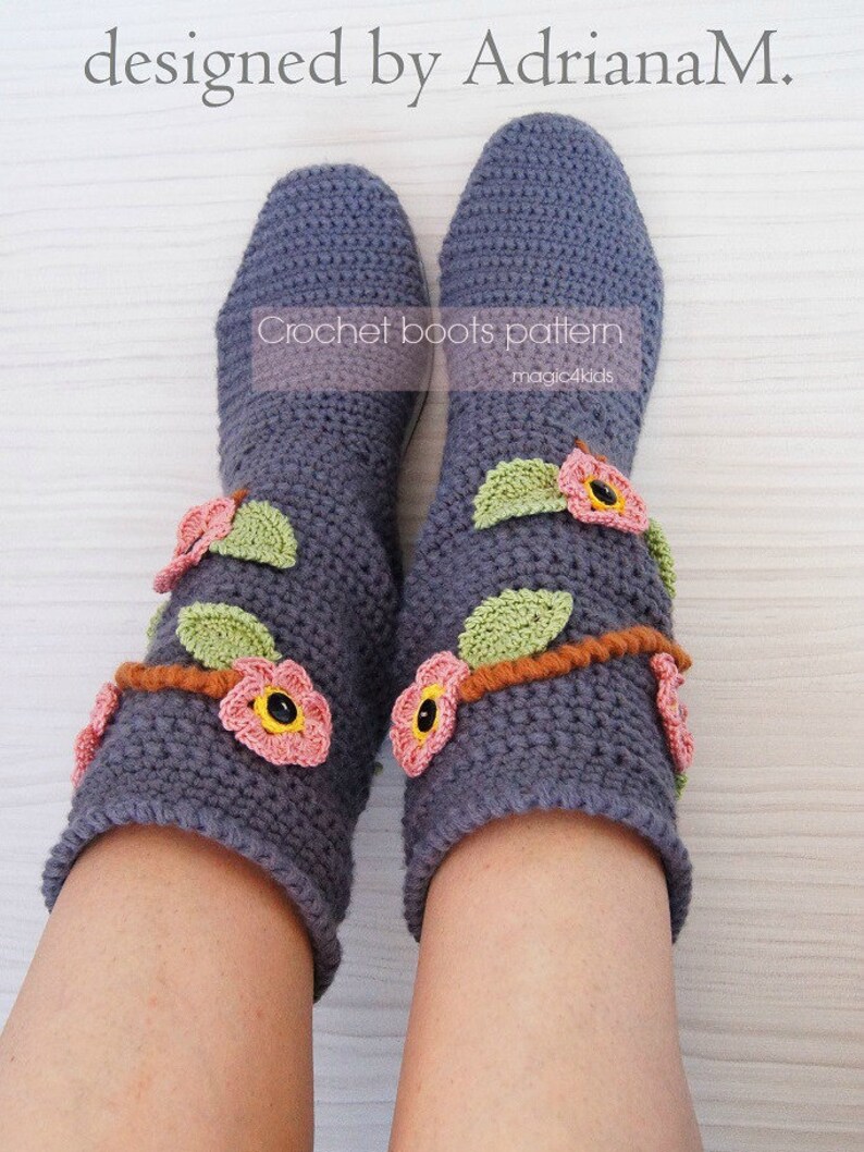 May include: A pair of gray crocheted boots with pink and green flower embellishments. The boots are designed by Adriana M. and are part of a crochet boots pattern by magic4kids.