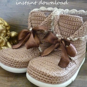 May include: A pair of brown crocheted booties with white soles and brown ribbon laces. The booties have a crocheted trim around the top. The text "***PDF Pattern*** instant download designed by Adrianam." is visible at the bottom of the image.