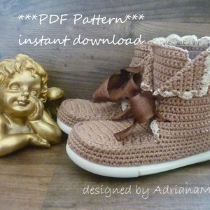 May include: Crochet pattern for a pair of brown booties with white trim and a brown ribbon. The pattern is available for instant download. The text "***PDF Pattern*** instant download" is visible in the image. The text "designed by AdriannaM." is also visible in the image.