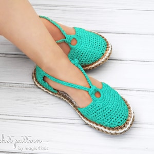 May include: A pair of teal blue crocheted sandals with a brown and white sole. The sandals have a strap that goes around the ankle and a small circle detail on the front.