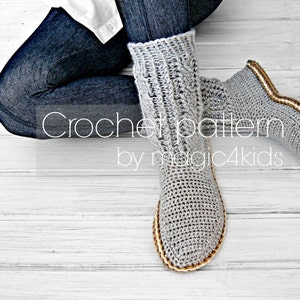 Puede incluir: Pantuflas de crochet grises con ribete marr&oacute;n y blanco. Las pantuflas las lleva puestas una persona sentada en un suelo de madera blanco. El texto "Crochet pattern by magic4kids" es visible en la imagen.