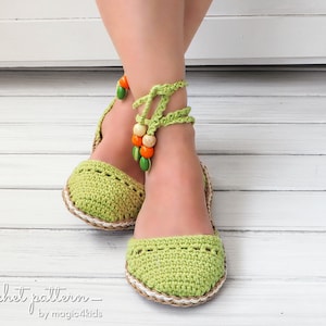 Puede incluir: Sandalias de ganchillo verdes hechas a mano con lazos en el tobillo y cuentas de madera decorativas. Las sandalias tienen una suela tejida y una puntera redondeada. El texto "_ crochet pattern _ by magic4kids" es visible.