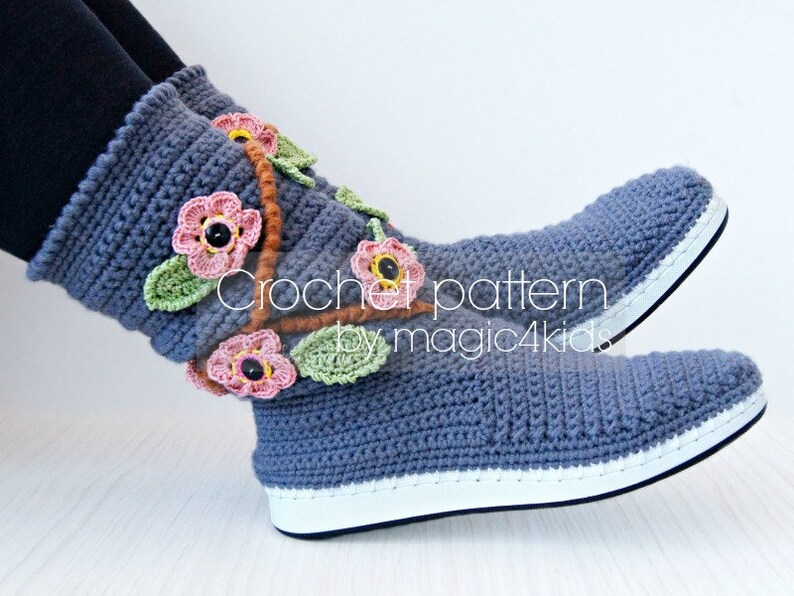 May include: Crocheted blue slippers with a white sole and floral embellishments. The flowers are pink, orange, and green. The text "Crochet pattern by magic4kids" is visible on the slippers.