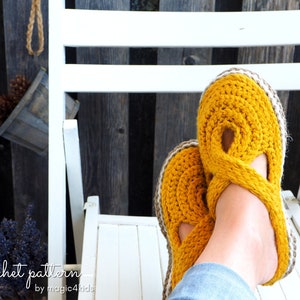 May include: A pair of yellow crocheted slippers with a brown trim. The slippers are worn by a person sitting on a white chair.