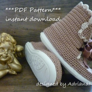 May include: Crochet pattern for a pair of brown booties with white trim and a brown ribbon. The pattern is available for instant download. The text "***PDF Pattern*** instant download" is displayed above the booties. The text "designed by AdrianaM." is displayed below the booties.