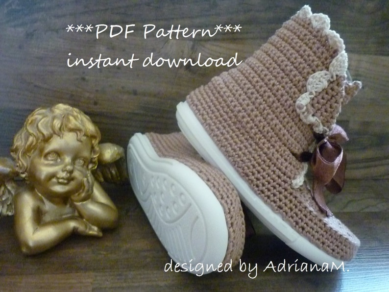 May include: Crochet pattern for a pair of brown booties with white trim and a brown ribbon. The pattern is available for instant download. The text "***PDF Pattern*** instant download" is displayed above the booties. The text "designed by AdrianaM." is displayed below the booties.