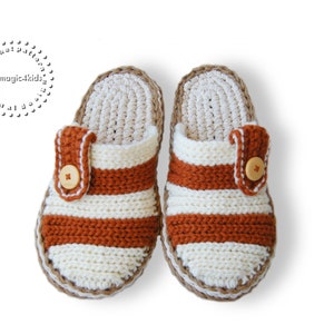 Può includere: Un paio di pantofole all'uncinetto con strisce marroni e bianche e un dettaglio a bottone. Le pantofole hanno una suola all'uncinetto.
