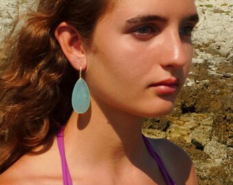 May include: A teardrop-shaped earring featuring a smooth, translucent light blue stone suspended from a thin metallic hook. The earring has a polished finish and a simple, elegant design that hangs vertically from the earlobe.