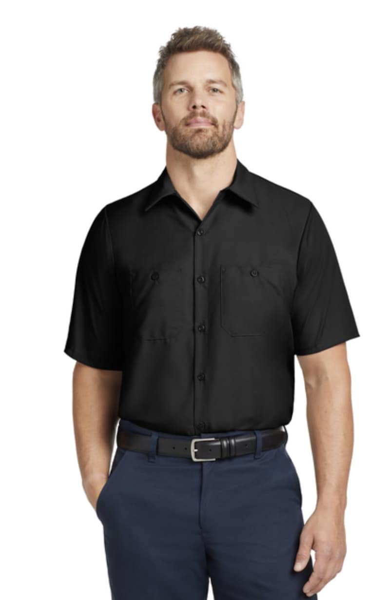 Puede incluir: Una camisa negra de manga corta con botones, cuello cl&aacute;sico y dos bolsillos en el pecho, combinada con pantalones azul oscuro y un cintur&oacute;n de cuero negro con una hebilla rectangular plateada, formando un conjunto de uniforme est&aacute;ndar.